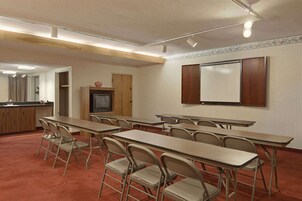 Un salón de conferencias con mesas, sillas, una televisión y una pizarra.