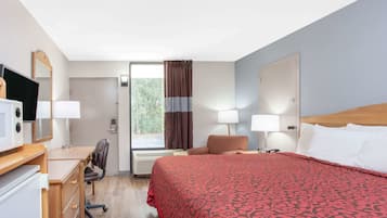 A hotel room with a bed, desk, chair, and a television.
