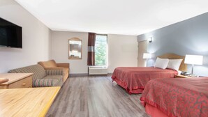 Hotellihuone, jossa on kaksi sänkyä, sohva, televisio ja ikkuna, jossa on verhot.