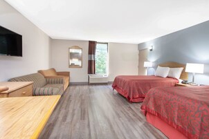 A hotel room with two beds, a sofa, a TV, and a window with curtains.