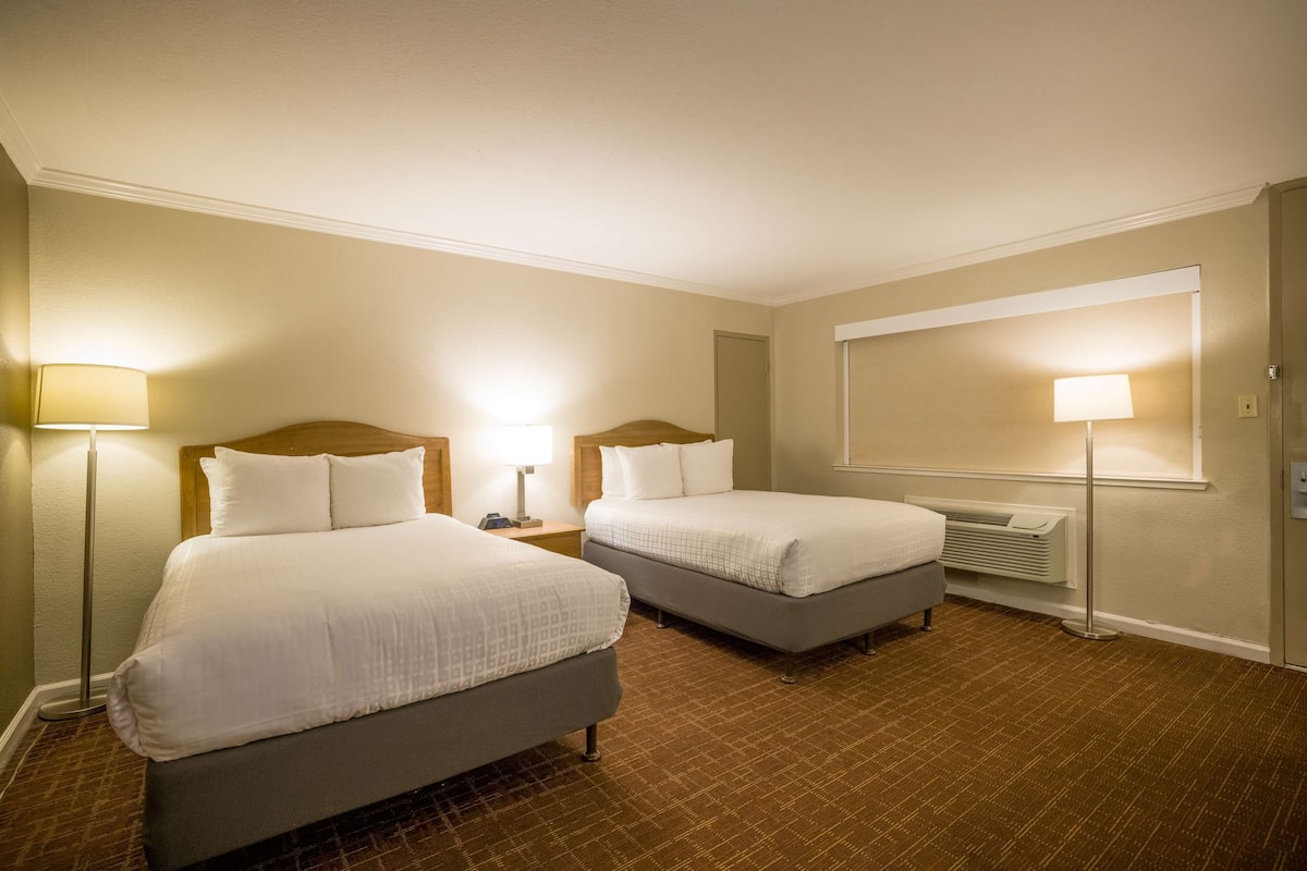A hotel room with two beds, a large mirror, and a standing lamp.
