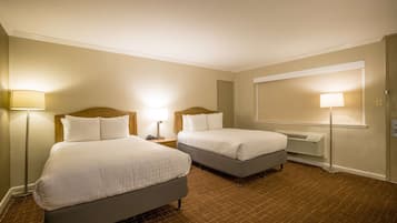 A hotel room with two beds, a large mirror, and a standing lamp.