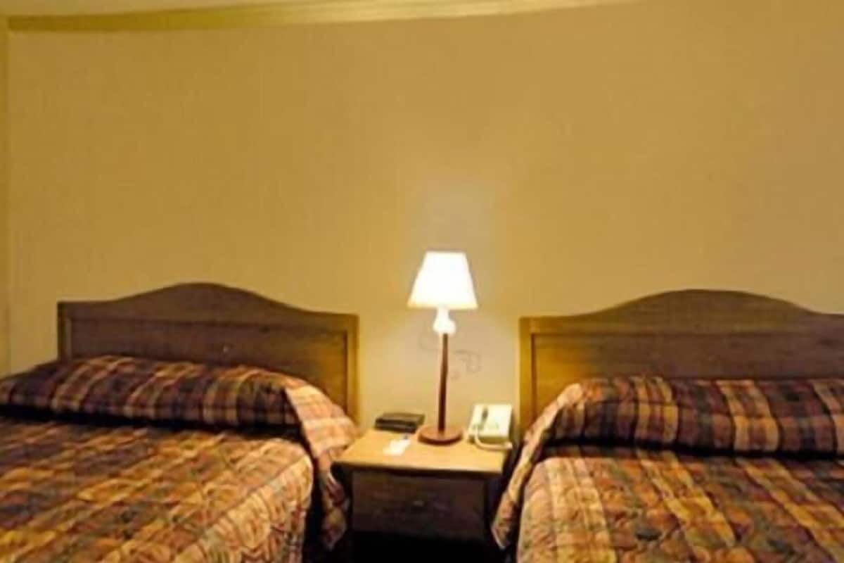 A hotel room with two beds, a nightstand, a lamp, and a telephone.