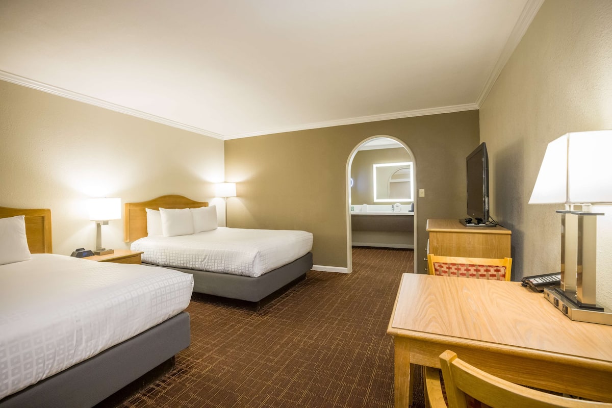A hotel room with two beds, a desk, a chair, a TV, and a mirror.
