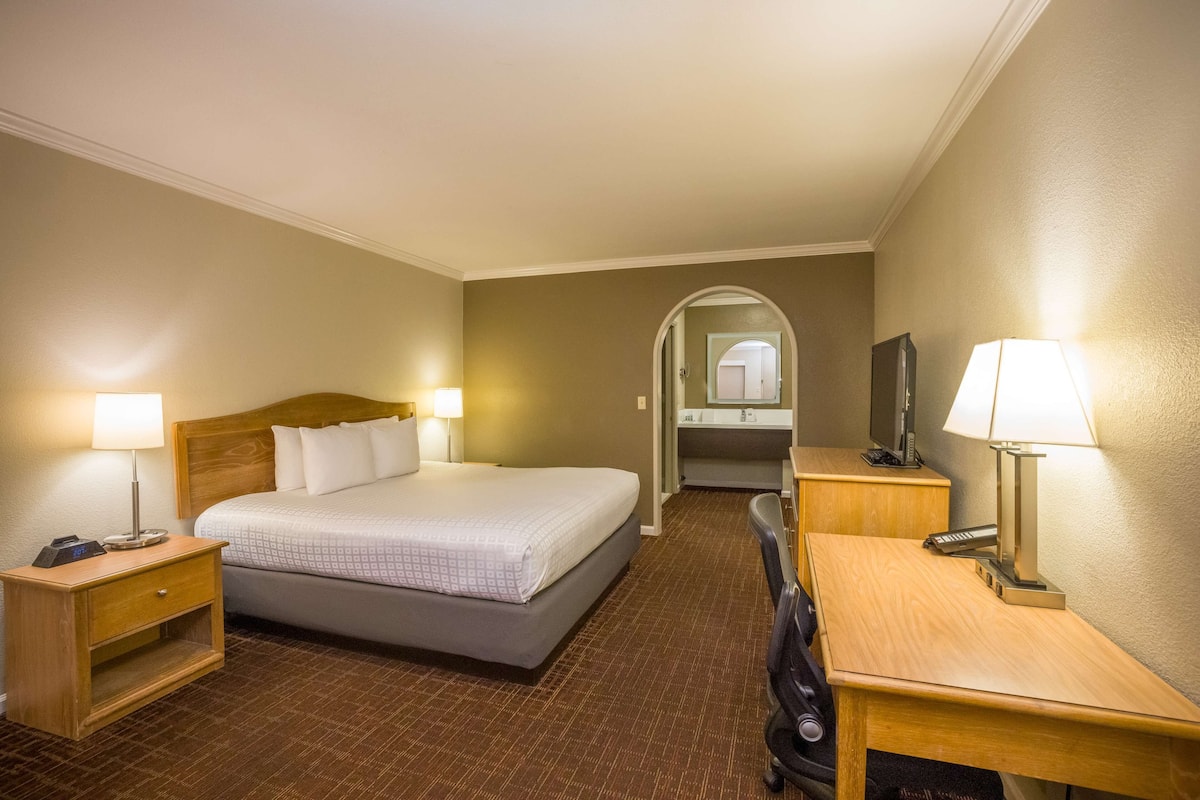 A hotel room with a bed, bedside table, desk, lamp, and a TV.