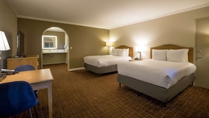 Ett hotellrum med två sängar, ett skrivbord, en stol, en spegel och ett badrum som syns genom en valvöppning.