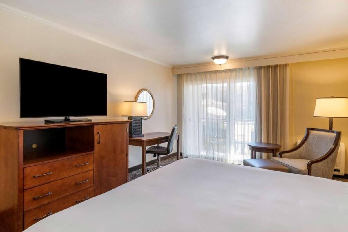 A hotel room with a bed, a desk, a television, a chair, a lamp, and a window with curtains.