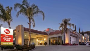 A hotel entrance with a sign for Best Western Plus, palm trees, and a parking area. - Best Western Plus Royal Oak Hotel (San Luis Obispo)