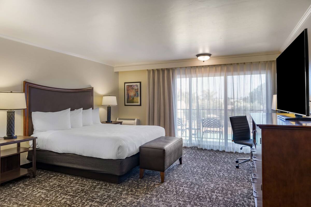 A hotel room with a large bed, a desk with a chair, a television, and a window with curtains.