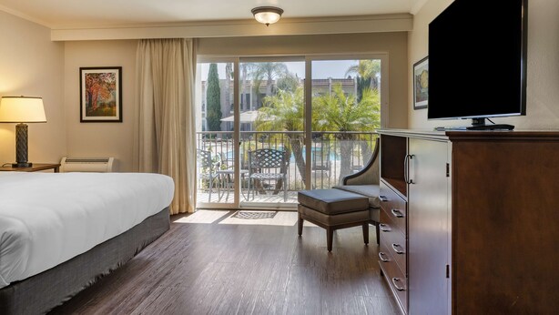 A hotel room with a bed, a TV, a desk, and a balcony with outdoor furniture. - Best Western Plus Royal Oak Hotel (San Luis Obispo)