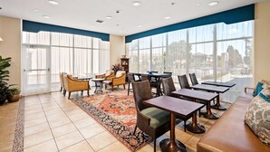 A spacious dining area with a large window, a patterned rug, and a variety of seating options including chairs and tables. - Best Western Plus Royal Oak Hotel (San Luis Obispo)