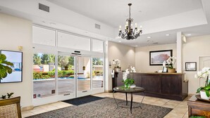 A hotel lobby with a reception desk, a chandelier, a large window, and a reception area with a plant. - Best Western Plus Royal Oak Hotel (San Luis Obispo)