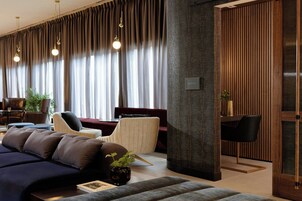 Una sala moderna con un sofá azul oscuro, un tablero de madera decorativo y un rincón de estar con un sofá rojo y un sillón blanco.