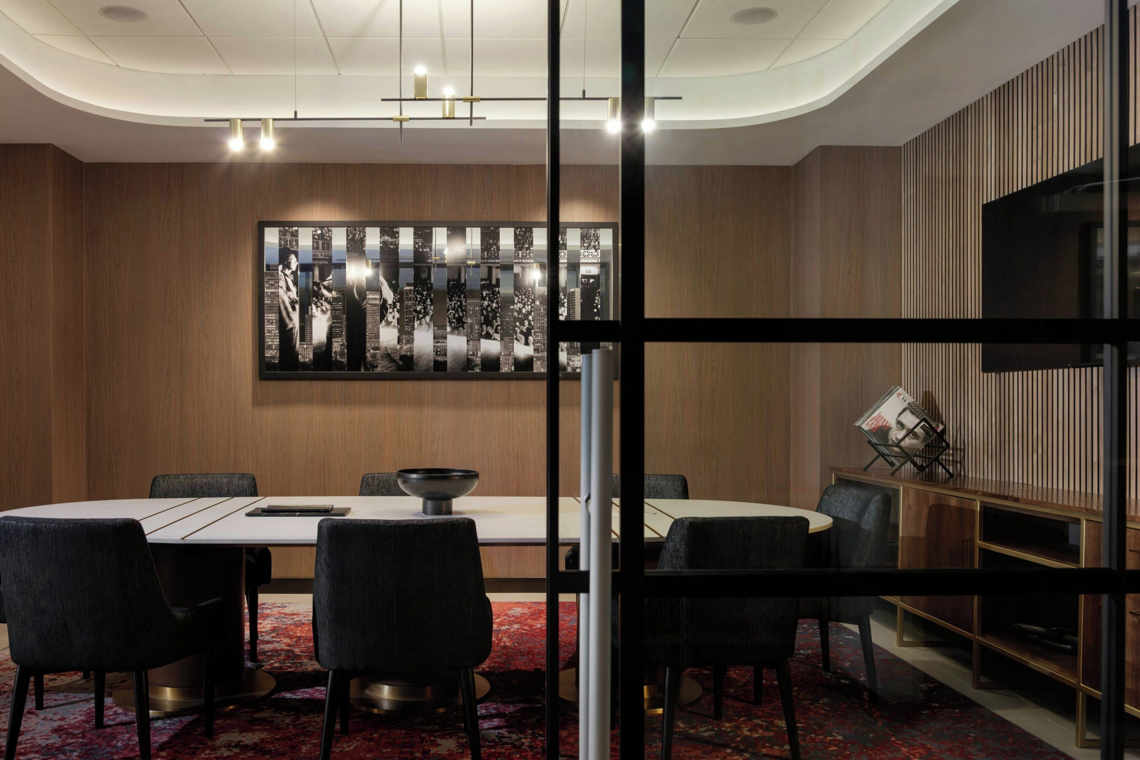 A modern conference room with a round table, black chairs, a large abstract artwork on the wall, and a television on a wooden panel.
