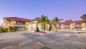 A hotel with a parking lot, multiple floors, and a red-tiled roof.