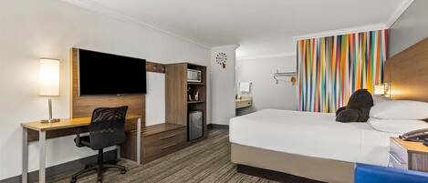 A hotel room with a bed, desk, chair, TV, and a colorful striped wall.