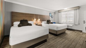 A hotel room with two beds, a wooden headboard, bedside lamps, a desk, and a window with curtains.