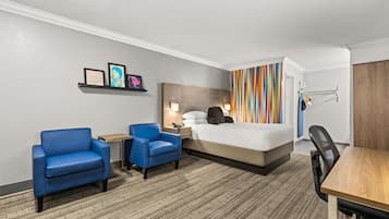 Ein Hotelzimmer mit einem Bett, zwei blauen Sesseln, einem Schreibtisch und einem Holztisch.