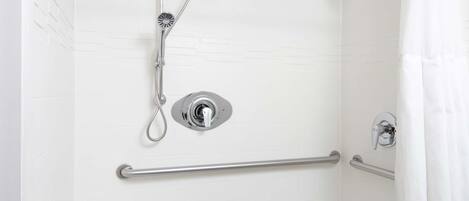 A walk-in shower with grab bars, a showerhead, and a small step stool.