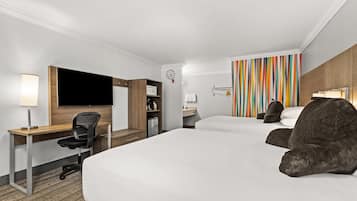Ett hotellrum med en stor säng, ett skrivbord med en stol, en tv, en mikrovågsugn och en vägg med färgglada ränder.