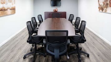 A conference room with a large table, six chairs, a TV on the wall, and artwork on the walls.