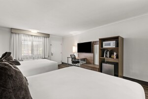 Una habitación de hotel con dos camas, un escritorio con silla, televisor, microondas y refrigerador.