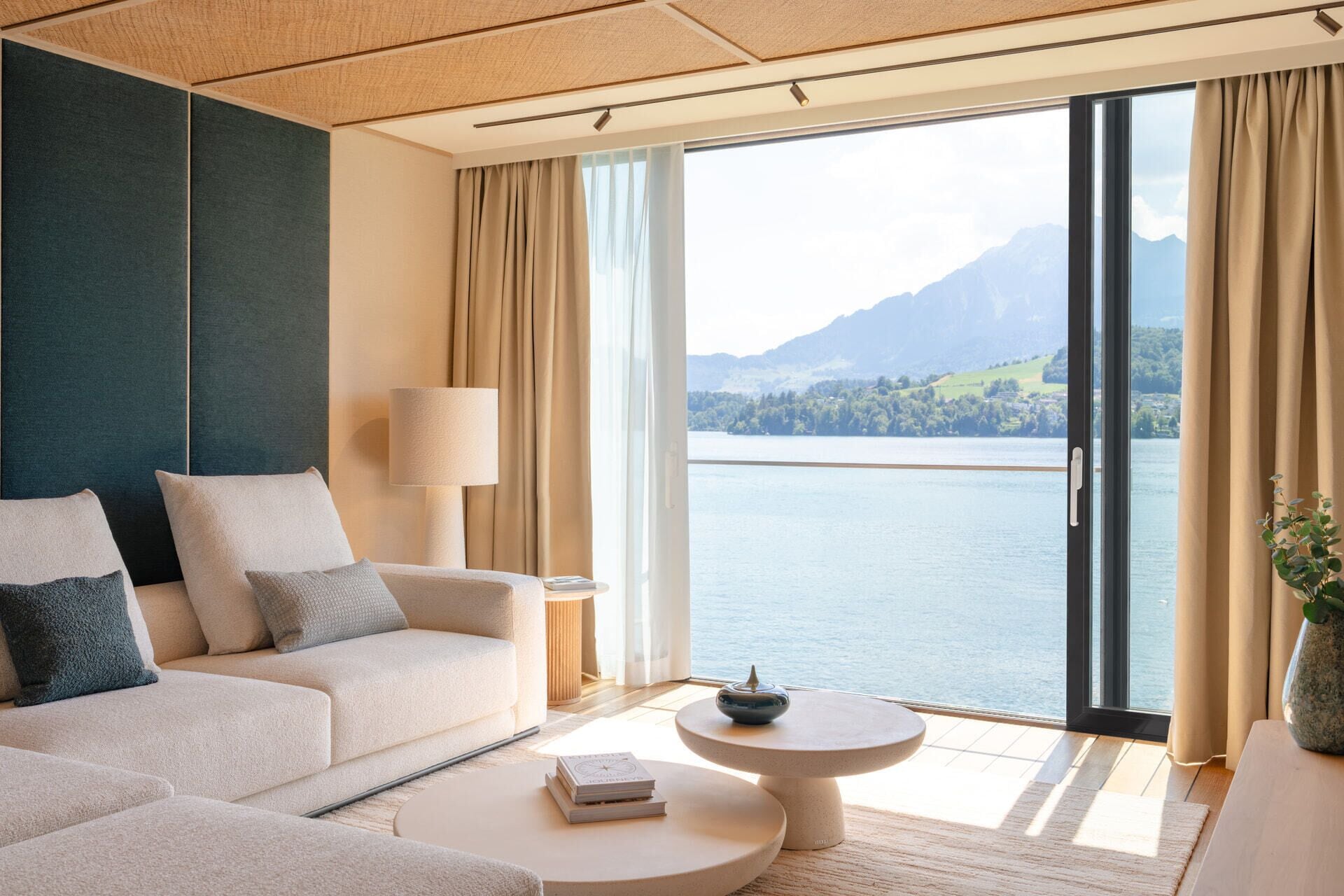 A modern living room with a sofa, a coffee table, and a view of a lake and mountains.