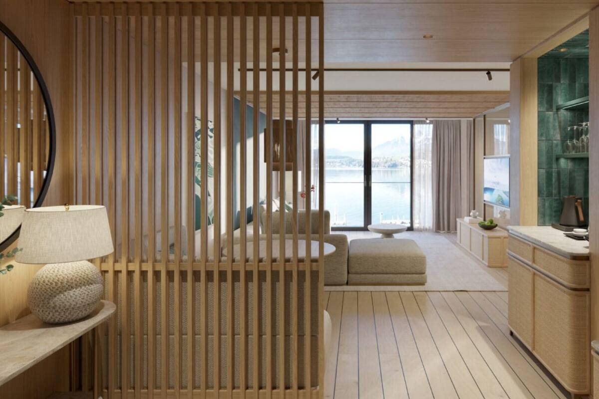 A modern hotel room with a wooden partition, a sofa, a dining area, and a view of the sea.
