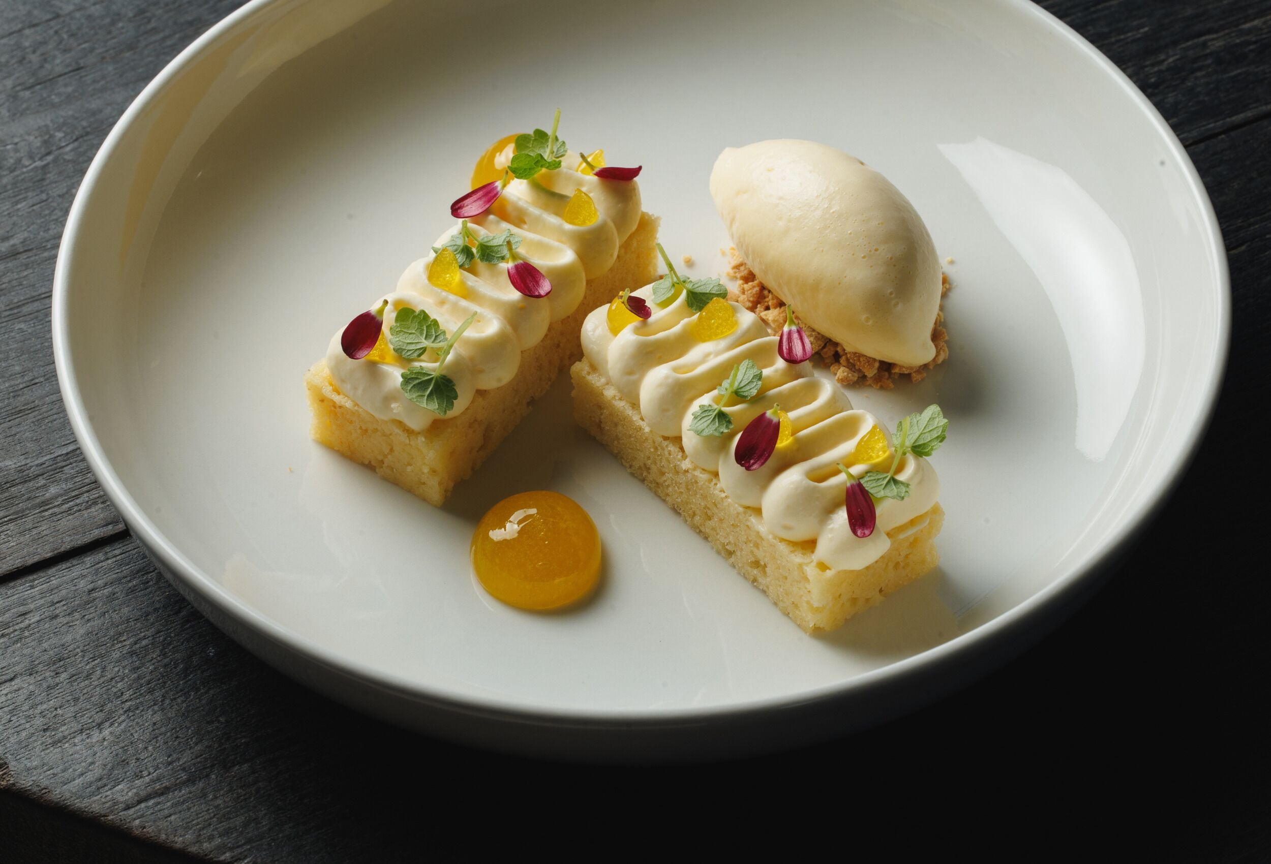 A dessert plate with two pieces of cake and a scoop of ice cream, garnished with edible flowers.