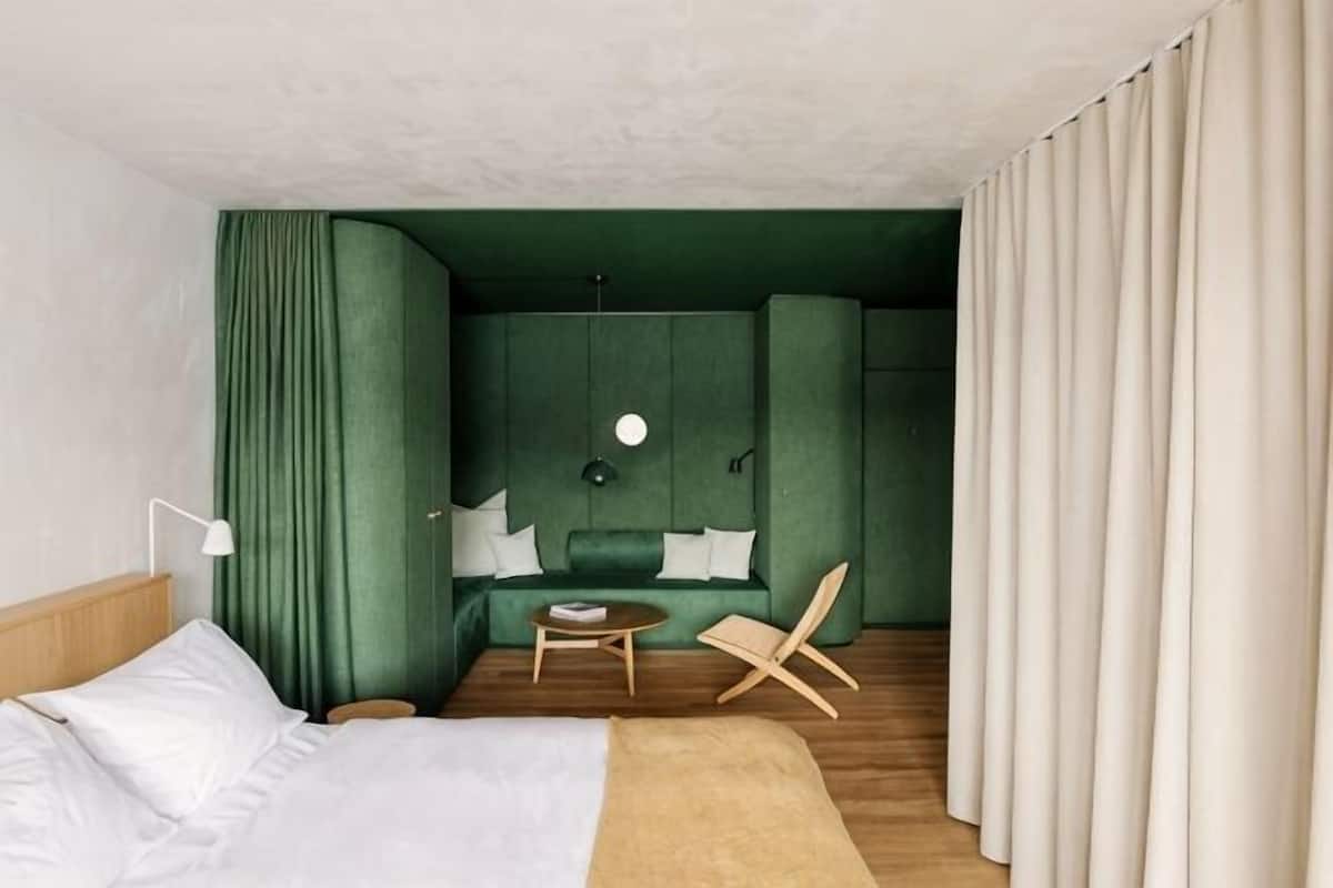 A hotel room with a bed, a small table, a chair, a sofa, and a green accent wall.