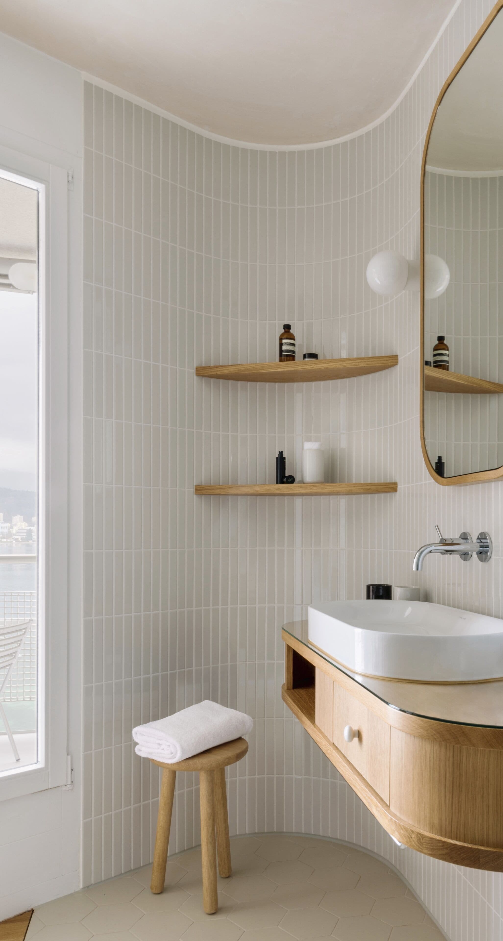 Un baño moderno con un lavabo blanco, estantes de madera y un espejo grande.
