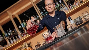 Ein Barkeeper gießt ein Getränk in ein Glas ein, im Hintergrund sind Regale voller Flaschen zu sehen.