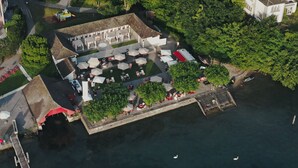 An aerial view of a riverside hotel with outdoor seating and a dock. - HERMITAGE Lake Lucerne - Beach Club & Lifestyle Hotel (Lucerne)