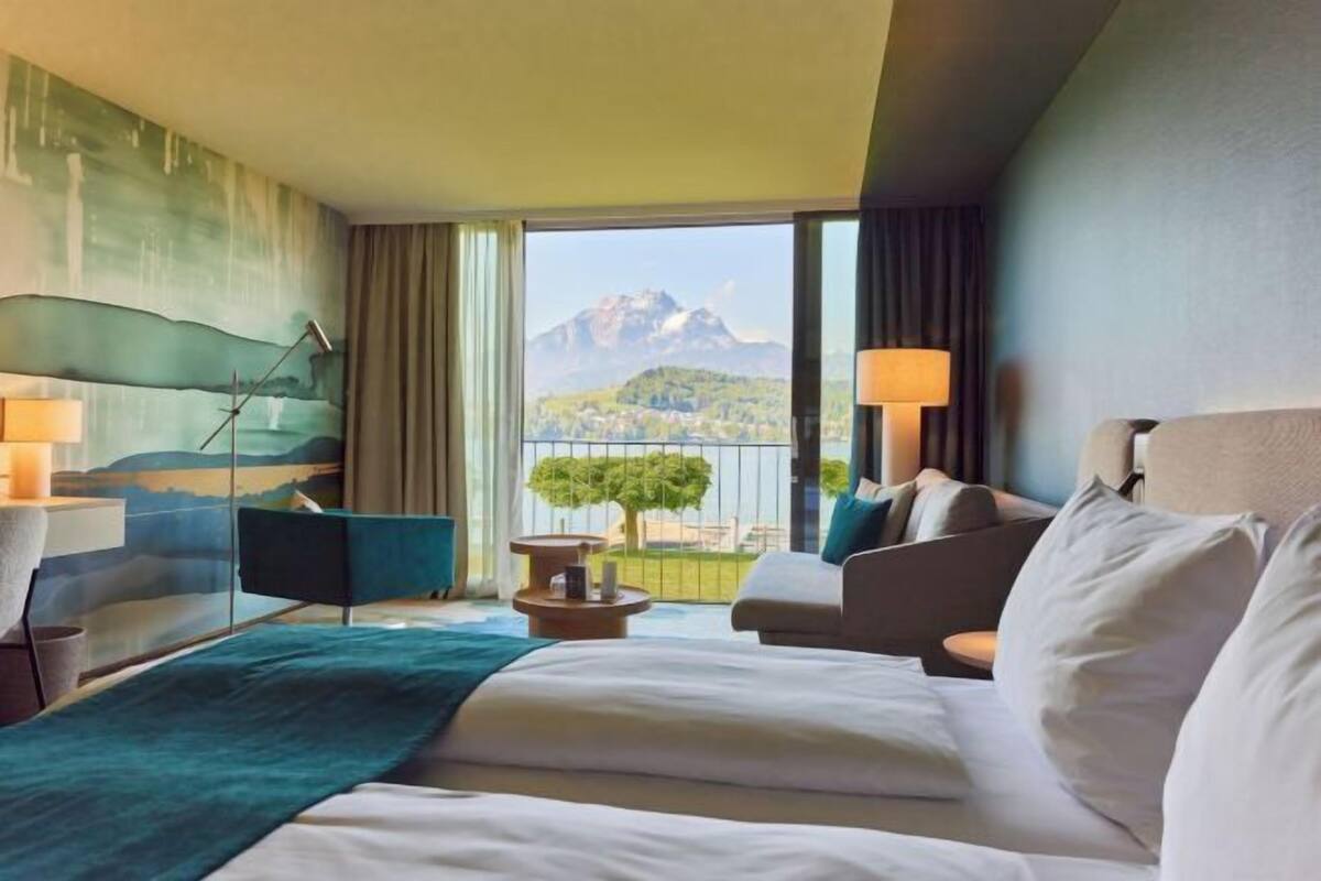 A hotel room with a bed, two chairs, a table, and a view of a mountain.