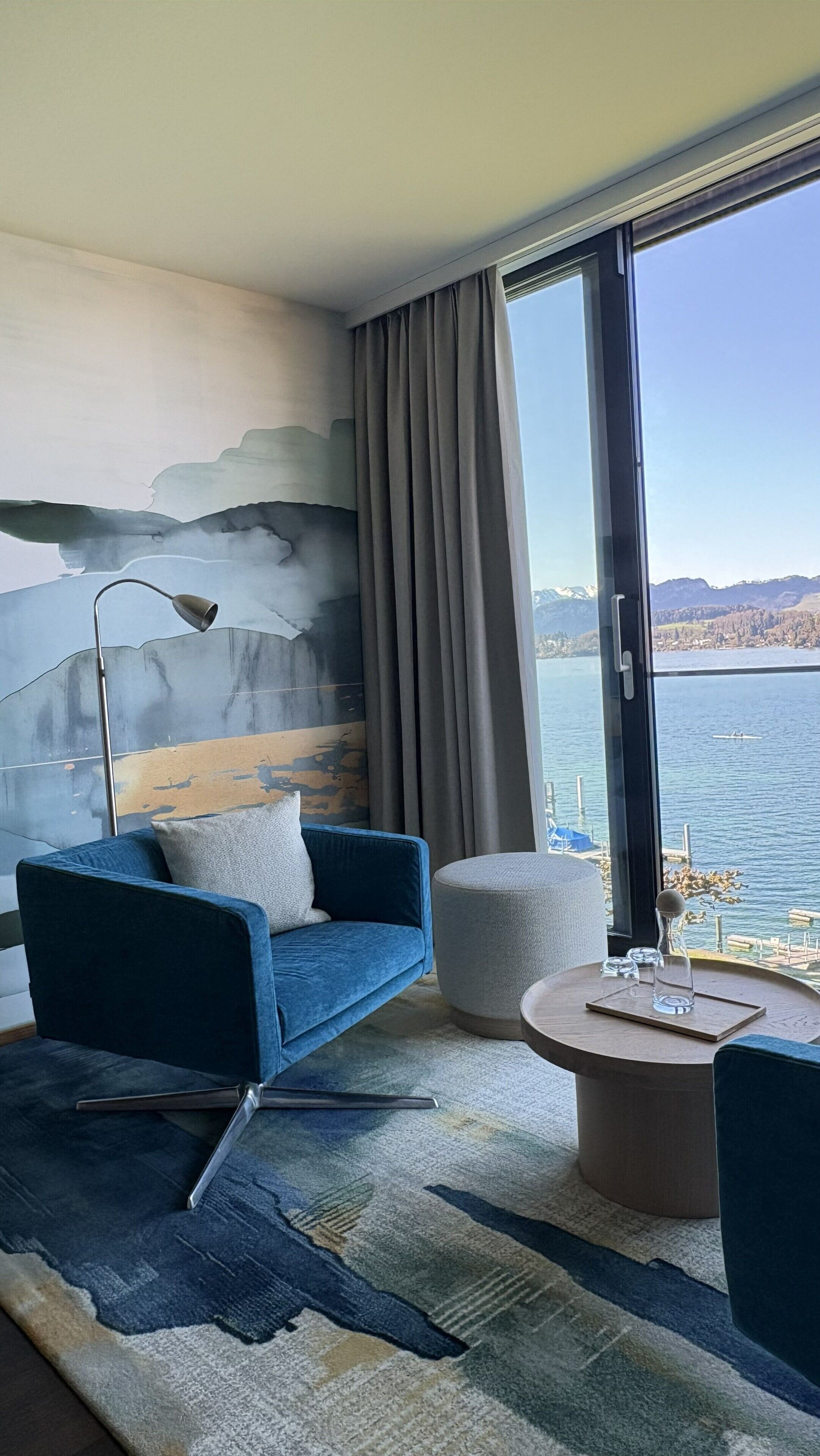 Ein modernes Zimmer mit einem blauen Sofa, einem runden Couchtisch, einer Lampe und Blick auf einen See.