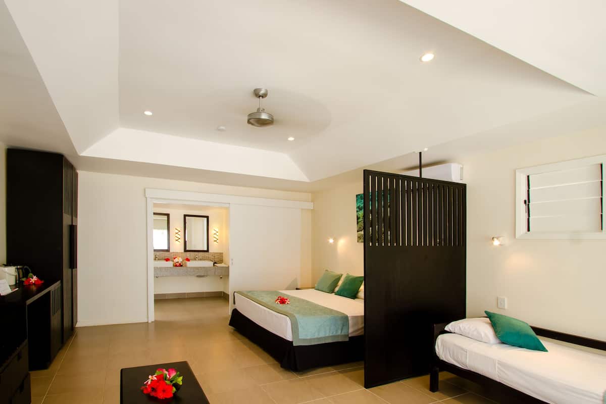 Une chambre d’hôtel moderne équipée d’un lit, d’un canapé, d’un bureau et d’une salle de bain, visible à travers une porte ouverte.