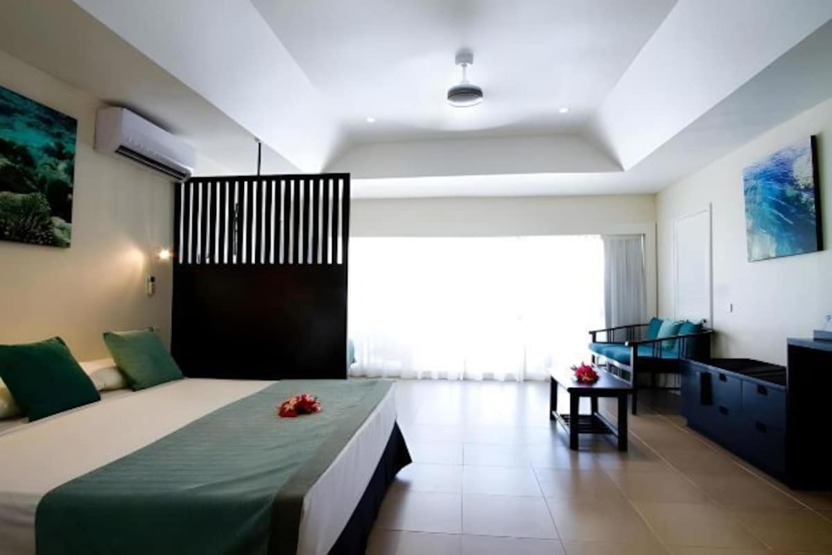 A modern hotel room with a large bed, a desk, and a view of the outdoors.