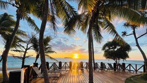 A wooden deck with lounge chairs and a railing overlooking a sunset over the ocean. - Nakelo Treasure Island Resort & Spa (Treasure Island)