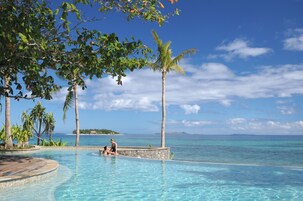 Zona de piscina con agua azul cristalina, rodeada de palmeras y vistas al océano.