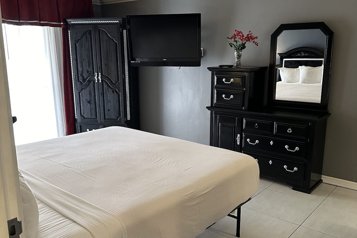 A bedroom with a bed, a dresser, a television, and a mirror.