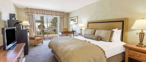 A hotel room with a large bed, a television, a desk, and a chair.