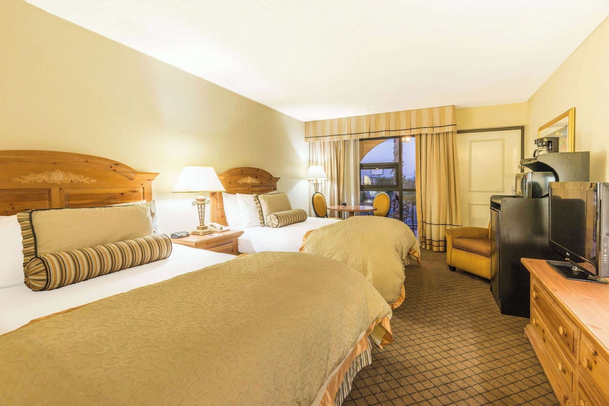 A hotel room with two beds, a TV, a desk with a lamp, and a view of the outside.