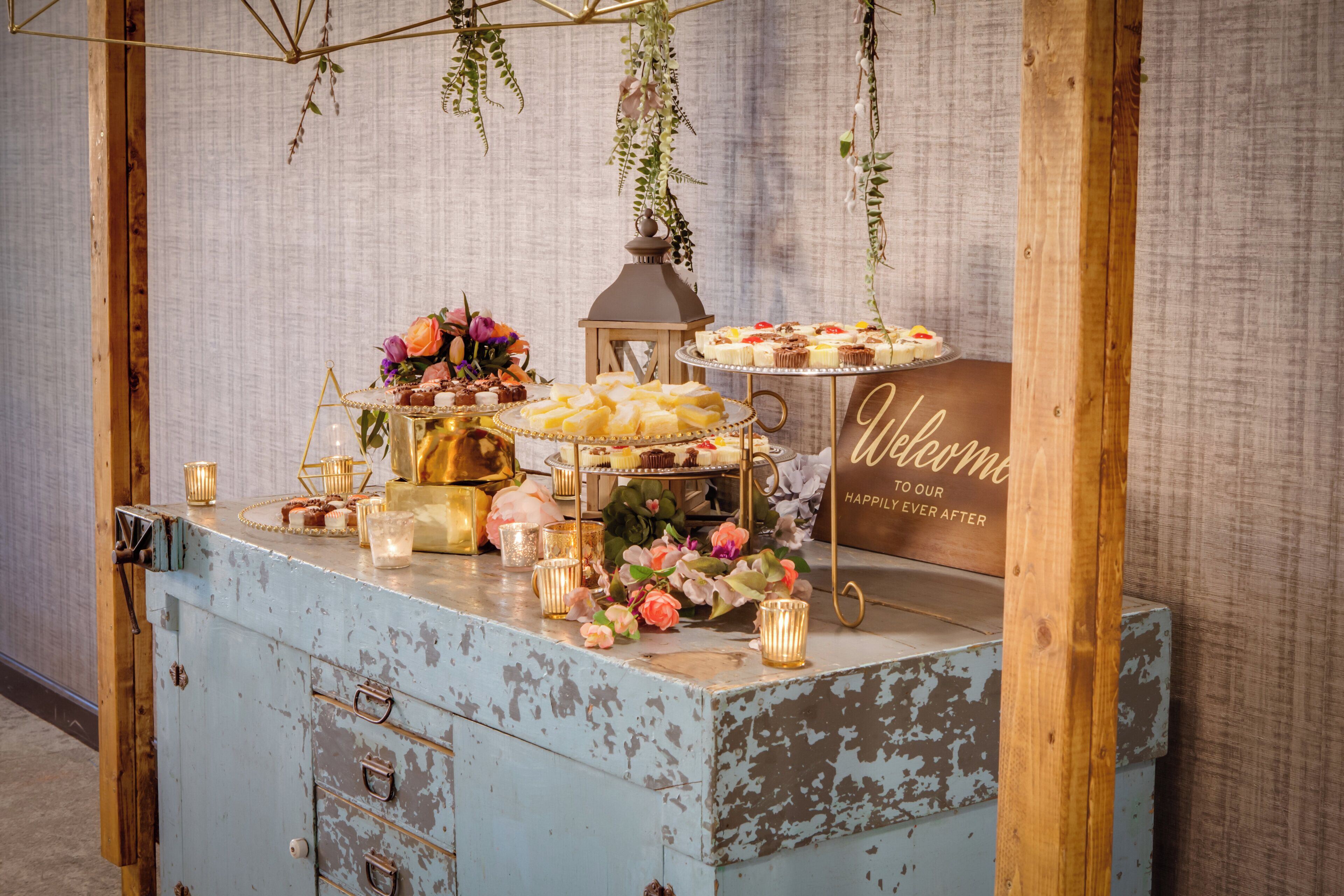 Un présentoir de desserts de style vintage, agrémenté d’une pancarte « Bienvenue », de bougies et de décorations florales.