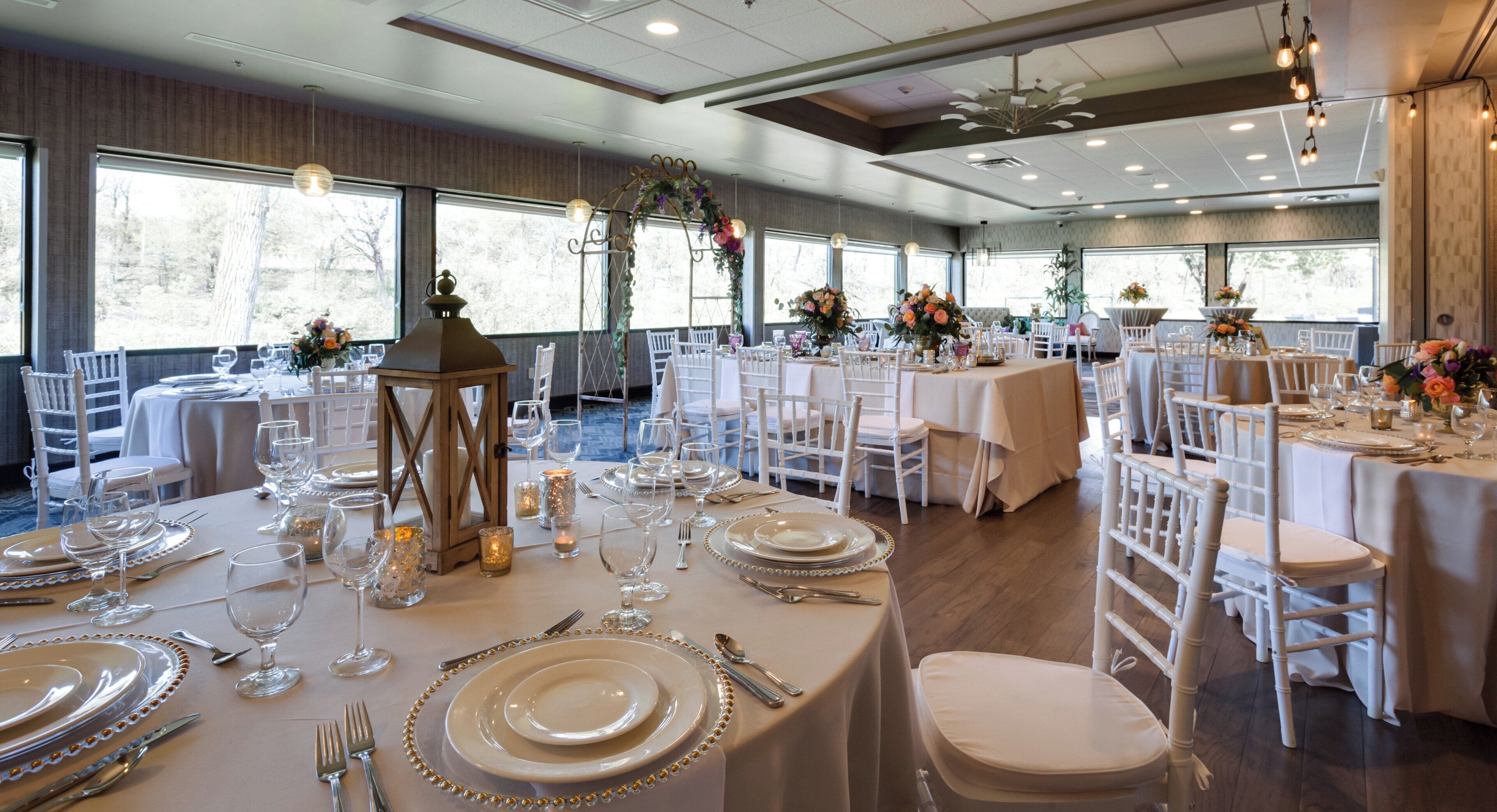 A banquet hall with round tables set for dining, white chairs, and floral centerpieces.