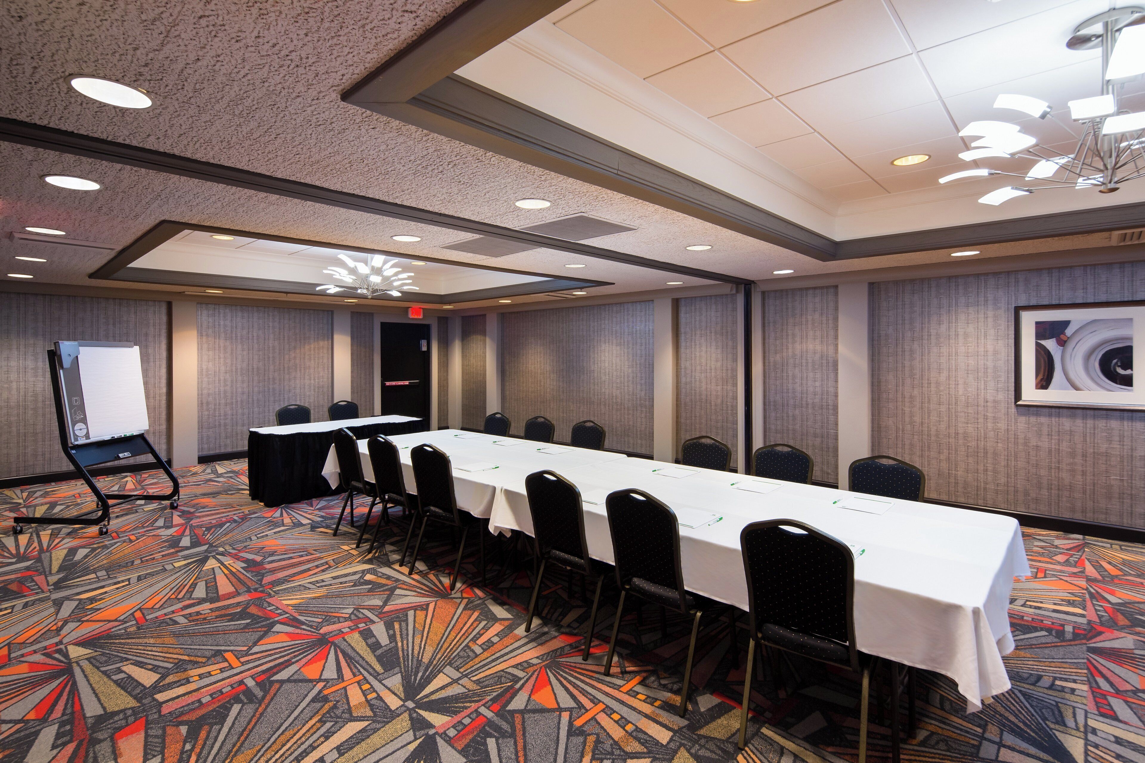 A conference room with a long table, chairs, a whiteboard, and a patterned carpet.