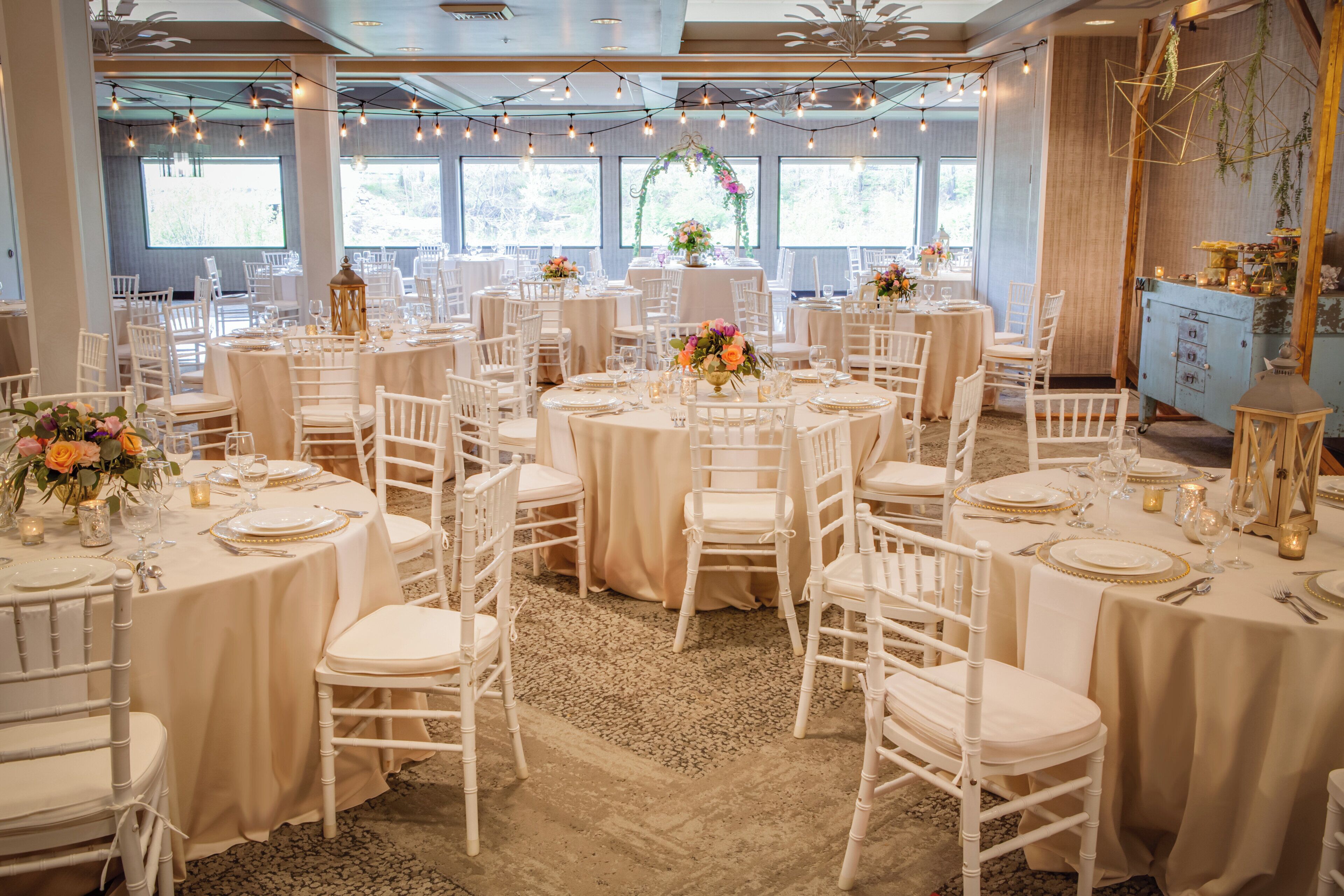 Une salle de banquet avec des tables rondes, des chaises blanches et des centres de table floraux.