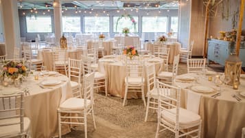 Une salle de banquet avec des tables rondes, des chaises blanches et des centres de table floraux.