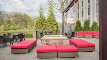 Un espacio de patio al aire libre con mobiliario de mimbre, cojines rojos y un hogar de piedra.