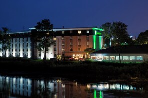 A hotel with a pool in the foreground, a restaurant with outdoor seating, and a building with a green sign.