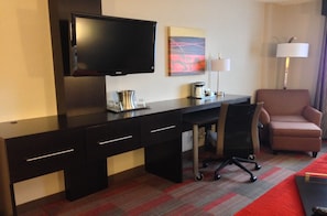 Une chambre d’hôtel équipée d’un téléviseur à écran plat fixé au mur, d’un bureau avec une chaise, d’une machine à café et d’une lampe.